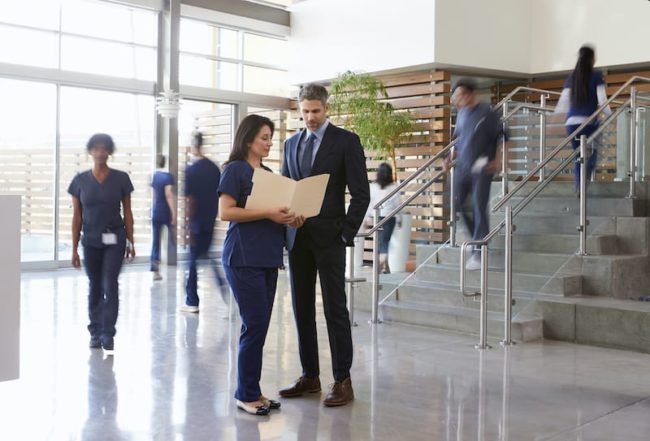 Two healthcare leaders talk in the lobby of a busy hospital